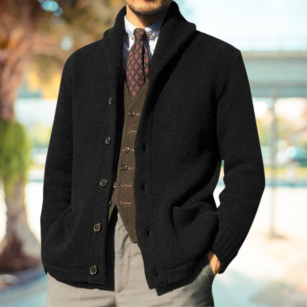 Giacca cardigan uomo nera elegante, abbinata a gilet marrone e cravatta a fantasia, perfetta per look autunnali e invernali. Moda maschile sofisticata.