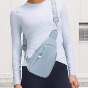 Maglietta bianca a maniche lunghe con marsupio azzurro, tracolla decorata, indossato da persona su sfondo bianco. Accessorio moda casual.