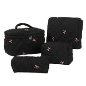 Set di borse da viaggio nere trapuntate con fiocchi rosa, include borsa grande, pochette, astuccio e borsa per cosmetici. Elegante e funzionale.