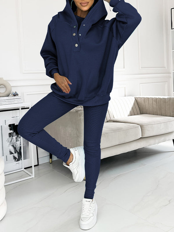 Donna in tuta sportiva blu navy, felpa con cappuccio e pantaloni aderenti, scarpe da ginnastica bianche, soggiorno moderno, moda casual.