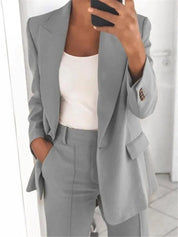 Donna in abito grigio elegante, giacca e pantaloni coordinati, indossa top bianco. Moda business casual, outfit professionale per ufficio.