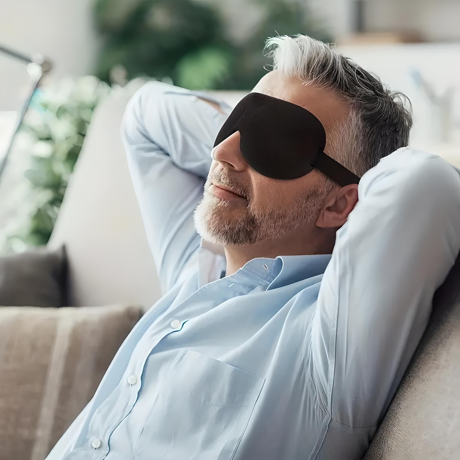 Uomo rilassato con maschera per dormire nera, seduto su divano. Riposo, relax, benessere. Ambiente domestico, luce naturale.
