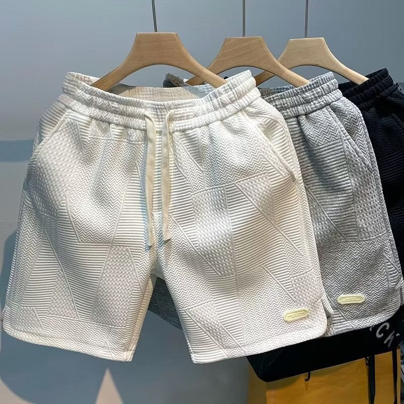Pantaloncini sportivi da uomo in cotone, colori bianco, grigio e nero, con motivo geometrico, elastico in vita e tasche laterali.