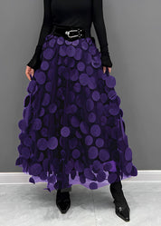 Gonna lunga viola con cerchi decorativi, cintura nera, indossata con maglia nera a maniche lunghe e stivali neri. Moda elegante donna.