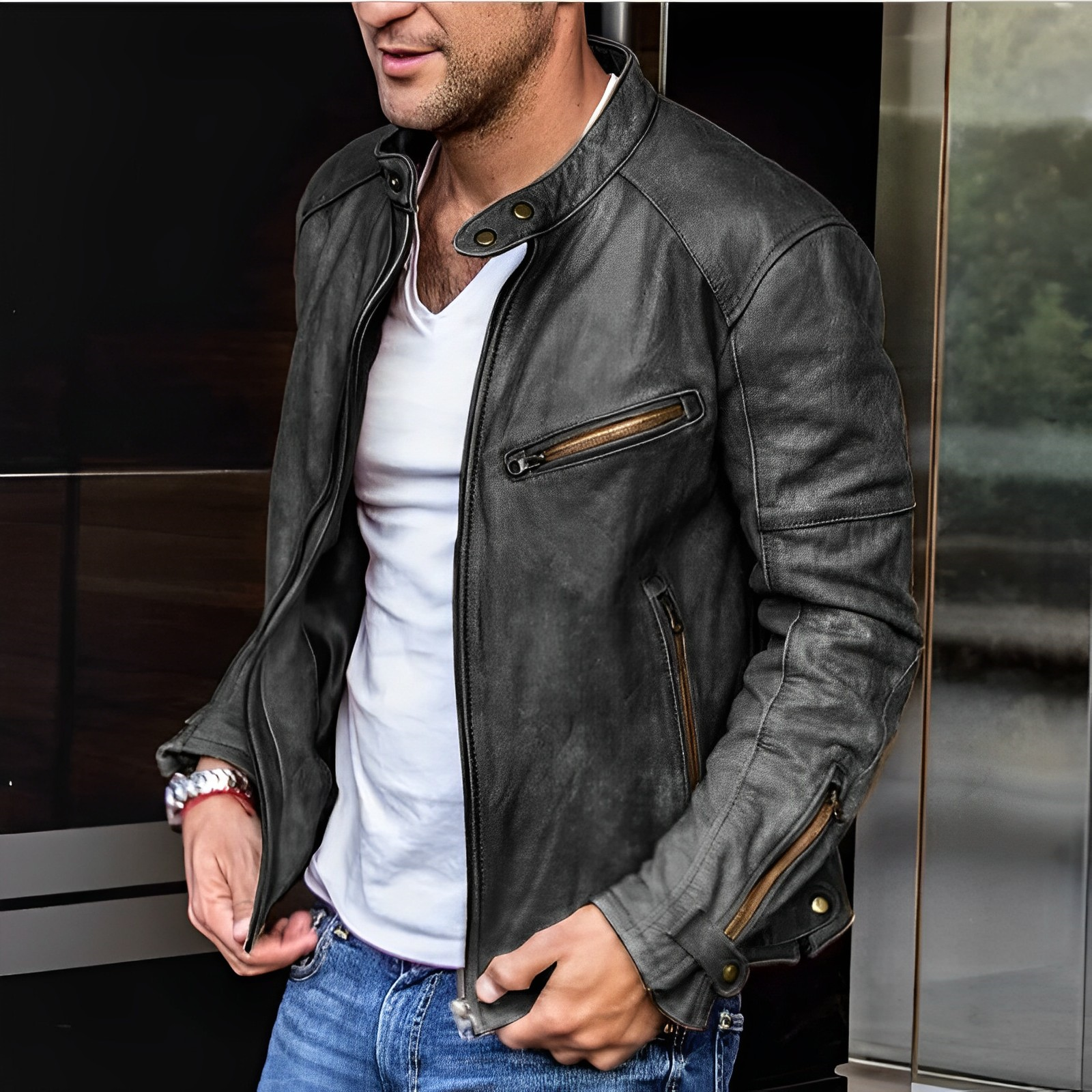 Giacca in pelle nera da uomo, stile motociclista, con zip e dettagli in metallo, indossata su t-shirt bianca e jeans. Moda casual maschile.