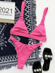 Bikini rosa a triangolo su tappeto blu con calendario 2021 e sandali neri con perle. Moda estiva, costumi da bagno donna, accessori mare.