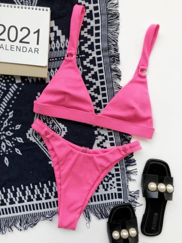 Bikini rosa a triangolo su tappeto blu con calendario 2021 e sandali neri con perle. Moda estiva, costumi da bagno donna, accessori mare.