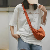 Donna con maglietta bianca oversize con scritta, borsa a tracolla arancione e cappello beige. Moda casual estiva, streetwear femminile.