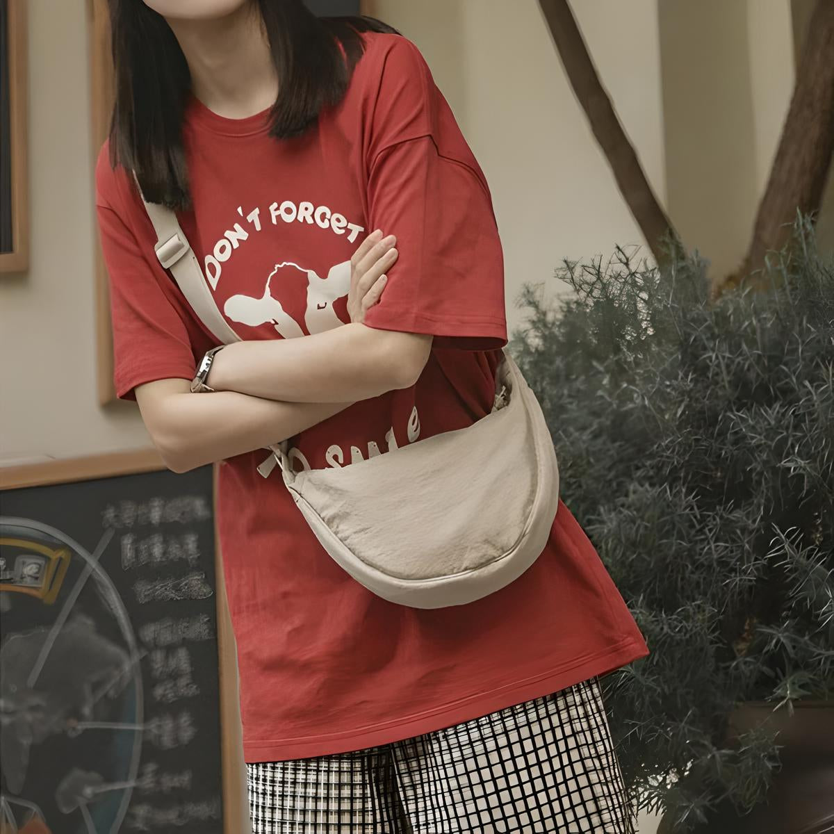 Donna con maglietta rossa grafica e borsa a tracolla beige, pantaloni a quadri. Moda casual, abbigliamento urbano, stile giovanile.