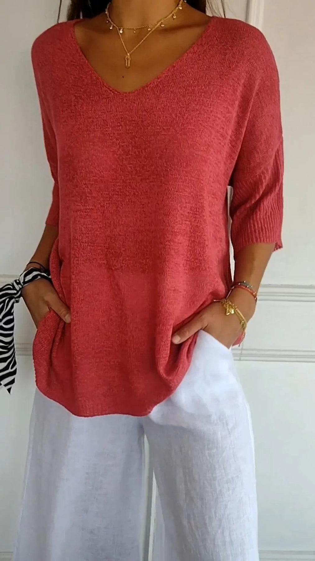 Maglia rosa a maniche corte con scollo a V, abbinata a pantaloni bianchi larghi. Look estivo casual, moda donna, abbigliamento leggero.