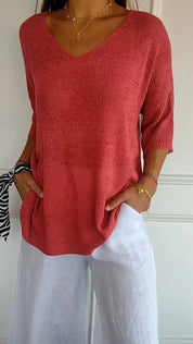 Maglia rosa a maniche corte con scollo a V, abbinata a pantaloni bianchi larghi. Look estivo casual, moda donna, abbigliamento leggero.