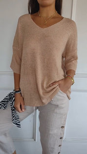 Maglia beige a maniche lunghe con scollo a V, abbinata a pantaloni chiari con bottoni laterali. Look casual ed elegante, moda donna autunno.