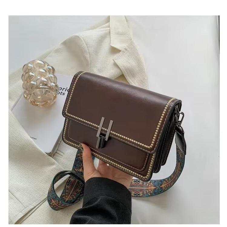 Borsa a tracolla in pelle marrone con dettagli metallici, su giacca beige. Accessorio moda elegante, perfetto per look casual e formali.