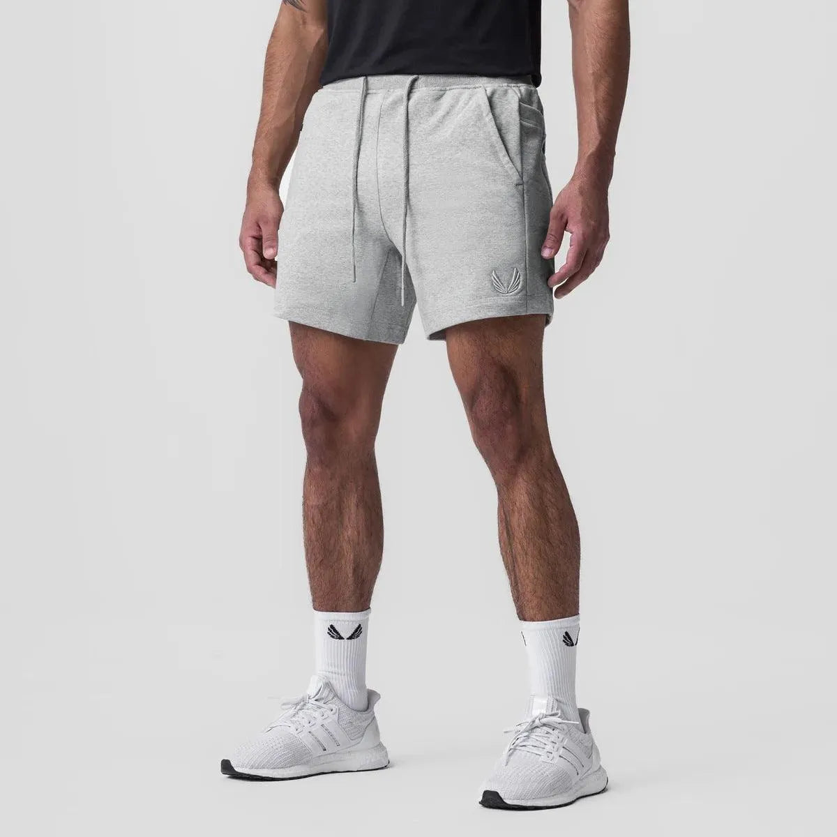 Pantaloncini sportivi grigi da uomo, con tasche e coulisse, abbinati a scarpe da ginnastica bianche e calzini, su sfondo neutro.