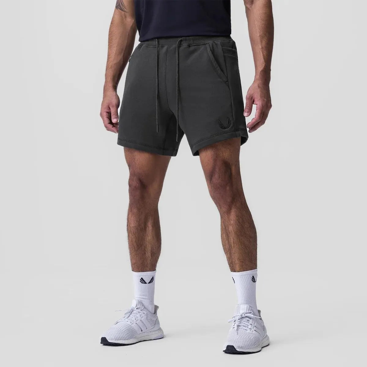 Shorts sportivi neri da uomo, con tasche e coulisse, indossati con scarpe da ginnastica bianche e calzini bianchi. Abbigliamento casual estivo.