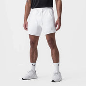 Shorts sportivi bianchi da uomo, con tasche e logo, indossati con scarpe da ginnastica bianche e calzini alti. Ideali per allenamento e tempo libero.
