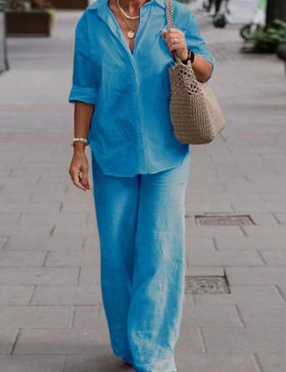 Donna con camicia e pantaloni blu, borsa a tracolla beige, cammina su marciapiede. Moda casual estiva, abbigliamento donna elegante.