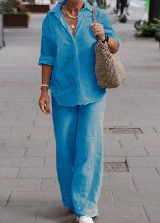 Donna con camicia e pantaloni blu, borsa a tracolla beige, cammina su marciapiede. Moda casual estiva, abbigliamento donna elegante.