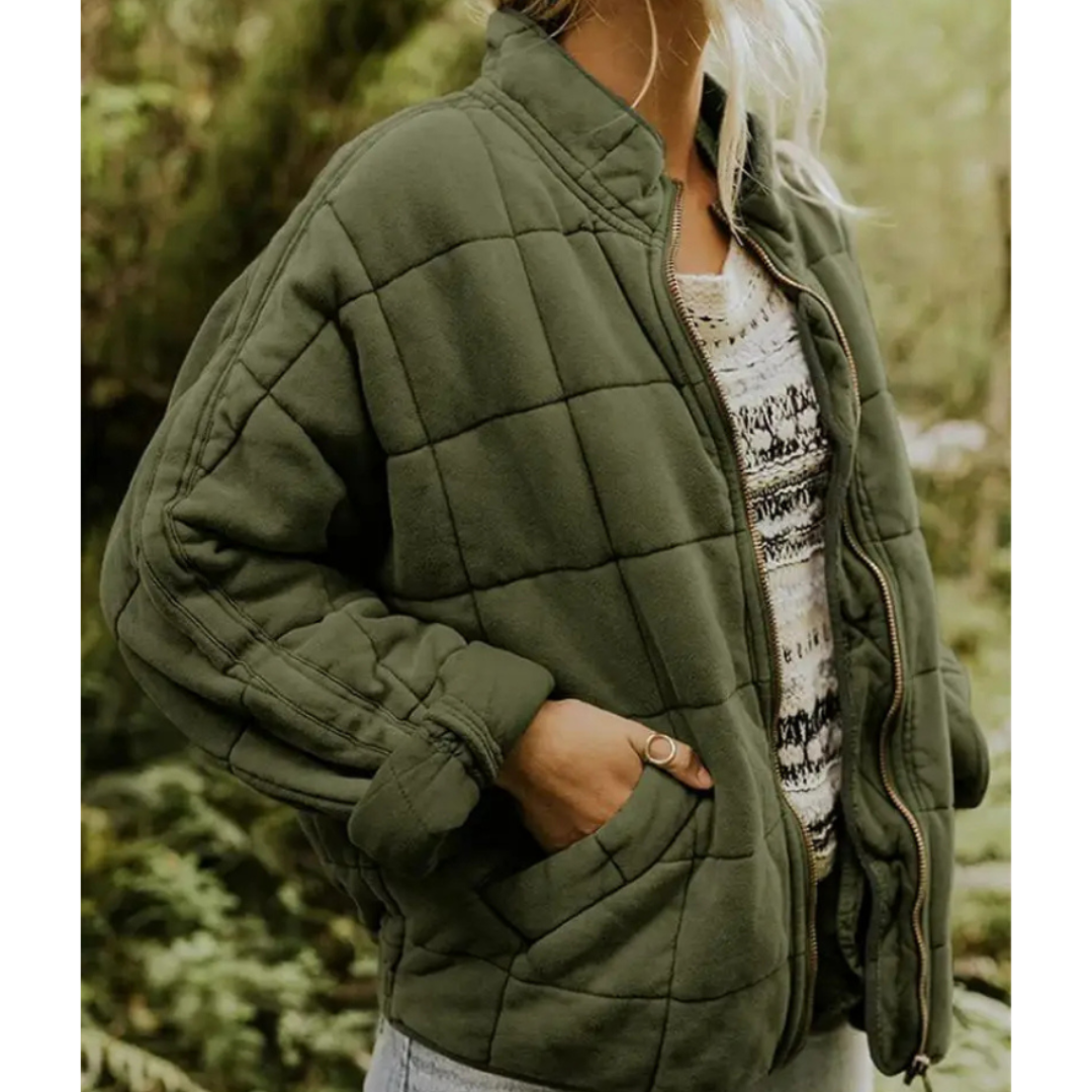 Giacca trapuntata verde oliva da donna, stile casual, con zip frontale e tasche laterali, indossata su maglia bianca a motivi.