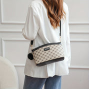 Donna con borsa a tracolla beige e nera con motivo geometrico, indossa giacca bianca e jeans. Accessorio moda elegante e versatile.