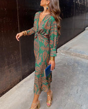 Donna con abito lungo verde a fantasia, sandali dorati e pochette blu. Moda elegante, abbigliamento femminile, stile autunnale.