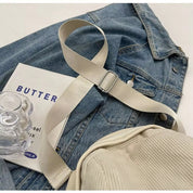 Giacca di jeans blu con cintura beige, borsa a coste e libro "Butter" su sfondo bianco. Accessori moda casual, stile urbano.