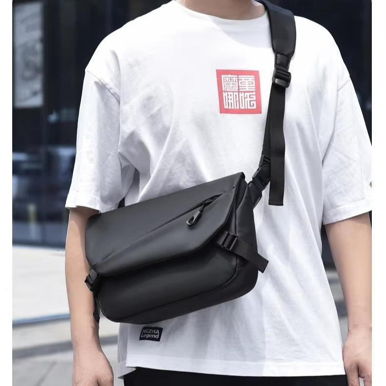 Uomo con borsa a tracolla nera in pelle, indossa maglietta bianca. Accessorio moda casual, ideale per lavoro e tempo libero.
