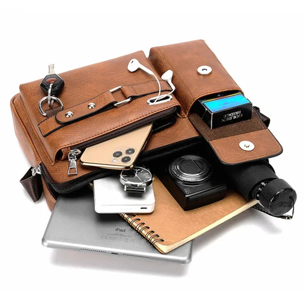 Borsa a tracolla in pelle marrone con tasche multiple, contenente smartphone, chiavi, auricolari, orologio, fotocamera, taccuino, iPad e ombrello.