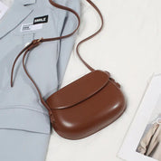 Borsa a tracolla in pelle marrone su giacca grigia, design elegante e minimalista, accessorio moda donna, perfetto per look casual e formali.
