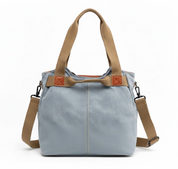 Borsa a tracolla in tela blu con manici marroni, dettagli in pelle, e tracolla regolabile. Design casual e spazioso, ideale per l'uso quotidiano.