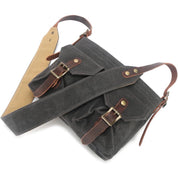 Borsa a tracolla in tela cerata grigia con dettagli in pelle marrone, fibbie in metallo, tasche frontali e tracolla regolabile. Elegante e resistente.