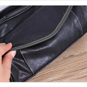 Borsa a tracolla in pelle nera con cuciture bianche, chiusura a zip, design elegante su sfondo in legno. Accessorio moda donna di alta qualità.