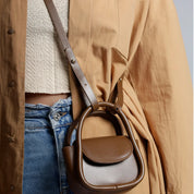 Borsa a tracolla marrone in pelle, design moderno, indossata su giacca beige e jeans. Accessorio moda donna, stile casual chic.