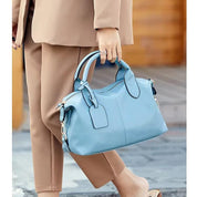 Donna con borsa a mano in pelle blu, elegante e moderna, indossa abito beige. Accessorio moda femminile, perfetto per look casual e formali.
