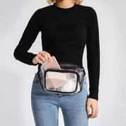 Donna con marsupio trasparente, indossa maglia nera e jeans. Marsupio contiene smartphone e accessori. Moda pratica, accessori trasparenti.