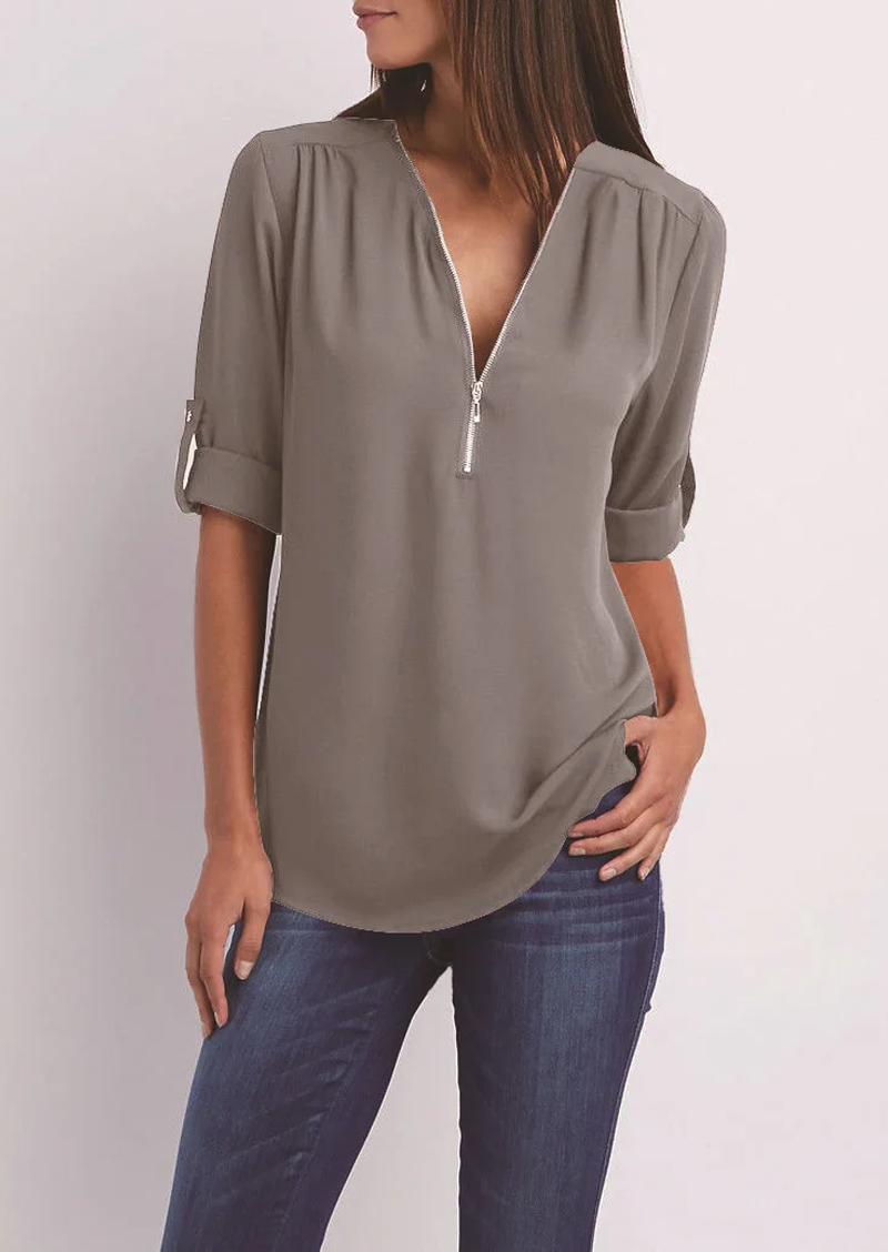 Blusa donna grigia con zip, maniche a 3/4 arrotolate, scollo a V, abbinata a jeans. Elegante e casual, perfetta per ogni occasione.