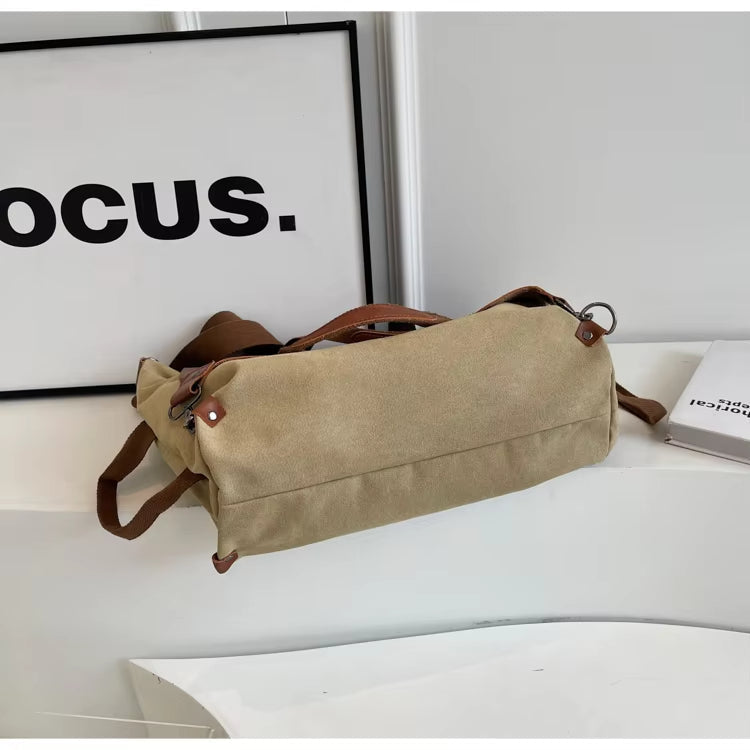 Borsa a tracolla in tela beige con dettagli in pelle marrone, posizionata su un tavolo bianco accanto a una cornice e un libro. Elegante e versatile.