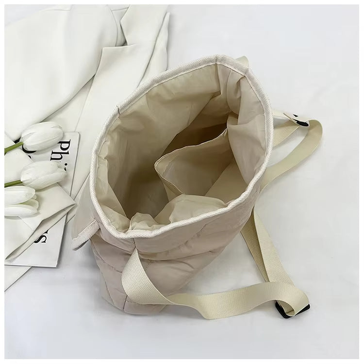 Borsa a tracolla beige in tessuto, aperta, con manici regolabili. Sfondo con tulipani bianchi e tessuto bianco. Design minimalista ed elegante.