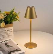 Lampada da tavolo dorata su tavolo bianco, accesa, con libri e fiori decorativi. Design moderno, illuminazione interna elegante.