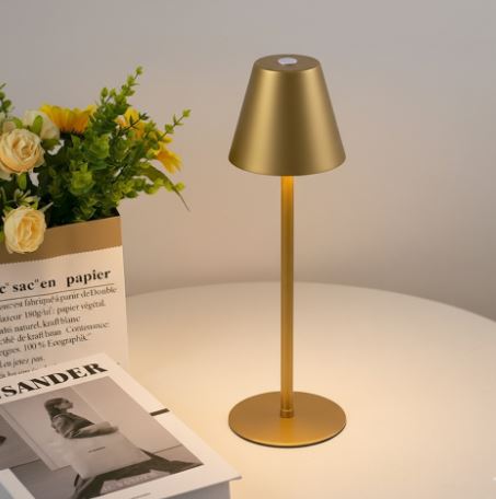 Lampada da tavolo dorata su tavolo bianco, accesa, con libri e fiori decorativi. Design moderno, illuminazione interna elegante.