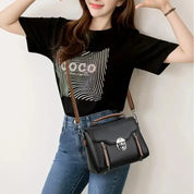 Donna con borsa a tracolla nera in pelle, indossa jeans e maglietta nera. Accessorio moda elegante, perfetto per look casual e quotidiani.