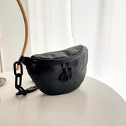 Marsupio nero in pelle su tavolo bianco, design moderno con cerniere e cinturino regolabile. Accessorio moda unisex, elegante e pratico.