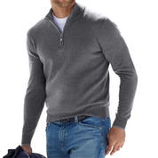 Maglione grigio da uomo con zip, indossato sopra una maglietta bianca, abbinato a jeans blu. Stile casual, moda autunnale, abbigliamento maschile.
