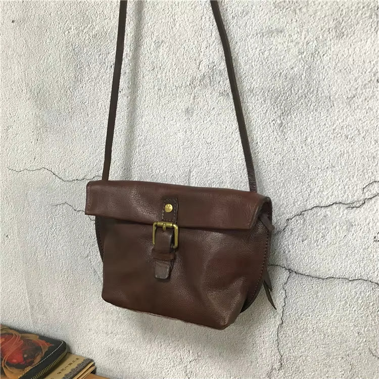 Borsa a tracolla in pelle marrone vintage, con fibbia dorata, appesa a parete. Accessorio moda elegante e pratico per ogni occasione.