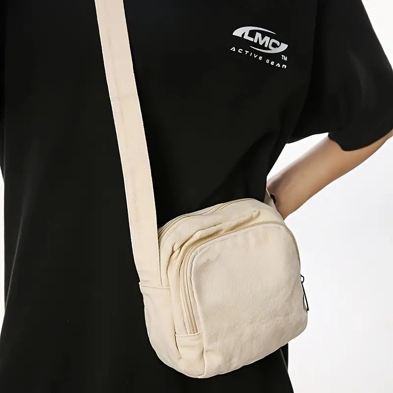 Borsa a tracolla beige in tessuto, indossata su maglietta nera. Design compatto, ideale per moda casual e accessori quotidiani.