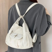 Zaino bianco in pelle su donna con giacca grigia, design moderno, tasca frontale con zip, ideale per moda urbana e viaggi.