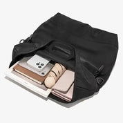 Borsa nera aperta con smartphone, libri, ombrello e portafoglio all'interno. Accessori moda, organizzazione, praticità quotidiana.