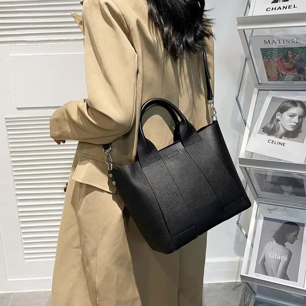 Donna con cappotto beige indossa borsa a tracolla nera in pelle, elegante e moderna, davanti a riviste di moda. Accessorio di tendenza per l'autunno.