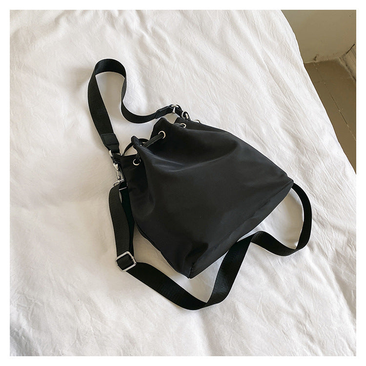 Borsa a tracolla nera su letto bianco, design minimalista, tessuto resistente, ideale per moda casual e quotidiana. Accessorio versatile ed elegante.