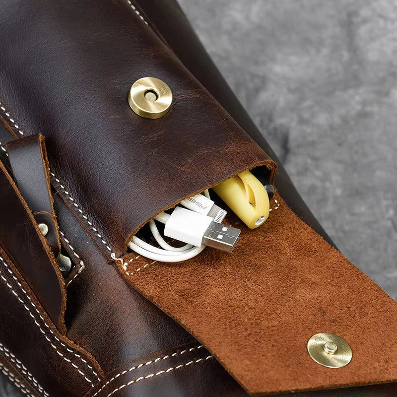Borsa in pelle marrone con tasca aperta, contenente cavi USB e accessori. Design elegante, cuciture bianche, chiusura a bottone dorato.